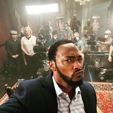 Anthony Mackie is taking a selfie as crew is working on the background.